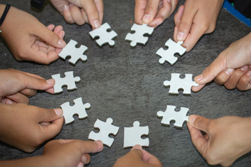 people helping in assembling puzzle, cooperation in decision making, team support in solving problems and corporate group teamwork concept, close up view of hands connecting pieces