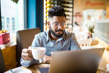 Young smiling indian man on laptop in cafe