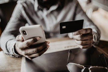 Canvas Print - Handsome young indian man with credit card and phone in hands doing purchases during online shopping