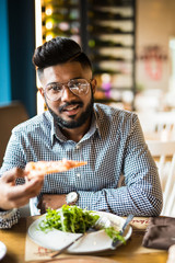 Wall Mural - Handsome indian man holding and eat piece pizza and salad in cafe