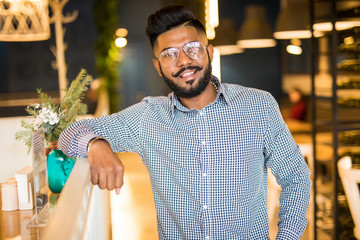 Wall Mural - Young indian hipster man standing indoors in cafe