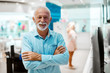 © dusanpetkovic1 - Smiling Caucasian senior man standing in tech store with arms crossed.