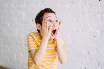 Cute tween surprised boy with funny face in yellow t-shirt isolated on white brick wall background