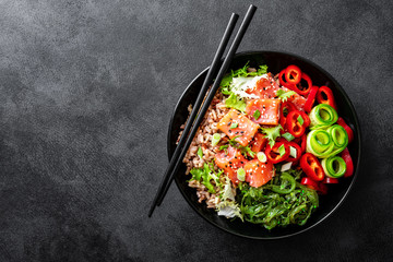 Canvas Print - poke bowl of brown rice, trout or salmon fillet, Chuka Seaweed Salad, sesame and fresh vegetables on dark background, top view, copy space, healthy food trend