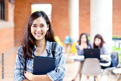 Fotomural Headshot of young happy attractive asian student smiling and looking at camera with friends on outdoor university background