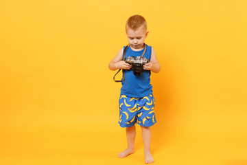 Wall Mural - Kid boy 3-4 years old in blue beach summer clothes hold retro camera isolated on bright yellow orange wall background children studio portrait. People childhood lifestyle concept Mock up copy space.