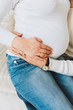 © Anastasiia - Husband and pregnant wife with their hands on the belly. Couple wearing white sweaters and jeans. Concept of pregnancy and expecting a baby.