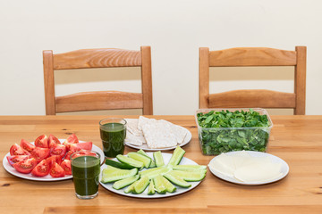 Wooden table with setting for two of healthy vegan vegetarian lunch or dinner green juice vegetables salad cucumbers, tomatoes in home