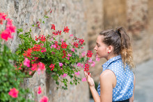 Monticchiello, Italy Town Or Village City In Tuscany Closeup Of Woman Young Girl Smelling Touching Red Flower Pots Decorations On Summer Day Stone Wall Architecture