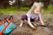 © MNStudio - Funny little girl playing in a large wet mud puddle on sunny summer day. Child getting dirty while digging in muddy soil.