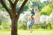 © MNStudio - Two cute sisters having fun on a swing in blossoming old apple tree garden outdoors on sunny spring day.