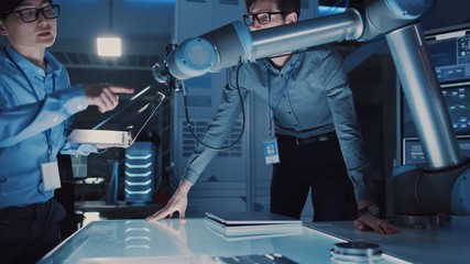 Leinwandbilder - Diverse Team of Engineers with Laptop and a Tablet Analyse and Discuss How a Futuristic Robotic Arm Works and Moves a Metal Object. They are in a High Tech Research Laboratory with Modern Equipment.