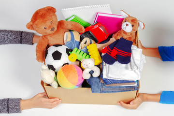 Wall Mural - Donation concept. Kid hands with donate box with clothes, books, school supplies and toys, white background