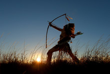 A Young Girl Plays The Part Of A Native American Indian Girl. She Poses Proudly In A Grassy Field In The Prairie The Girl Is Silhouetted As The Sun Sets Behind Her.