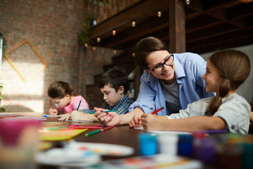 Portrait of smiling young woman working with kids in art class, copy space