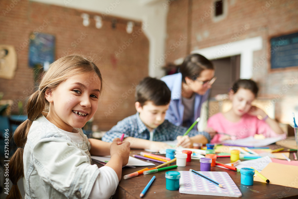 Portrait of cute little girl looking at camera while enjoying art class ...