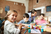 Portrait Of Cute Little Girl Looking At Camera While Enjoying Art Class With Group Of Children, Copy Space