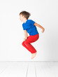 © epiximages - cool, cute boy with blue shirt and red trousers is jumping high in the studio in front of white background and white wooden floor