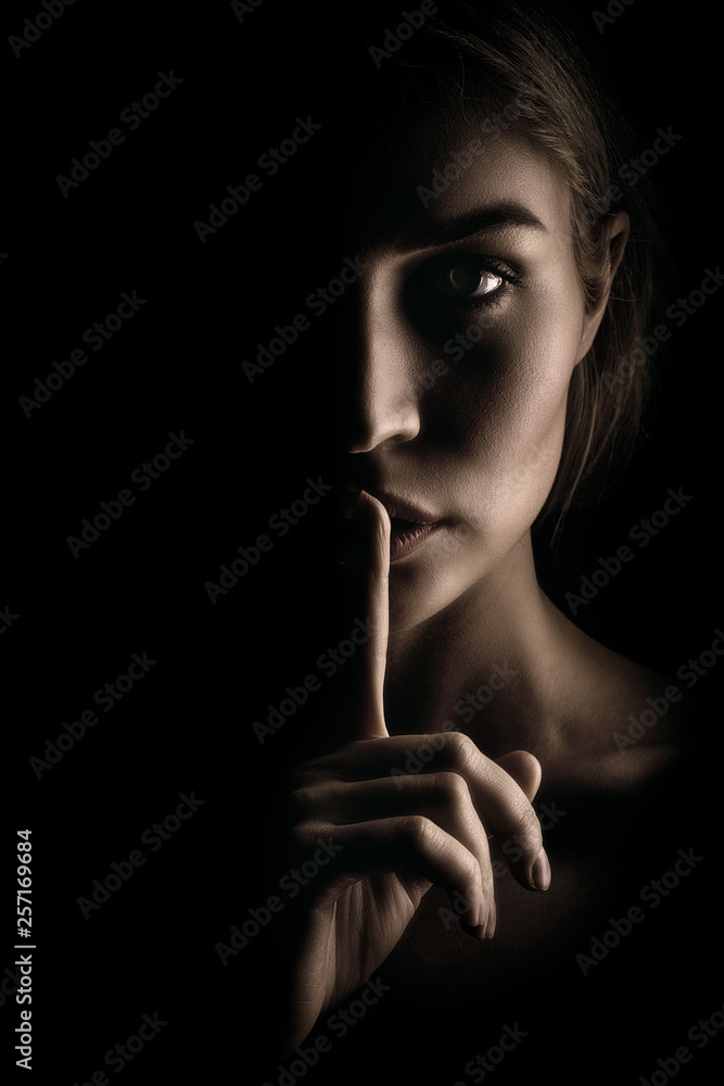 The girl shows a sign of silence. Face on black background, close-up - obrazy, fototapety, plakaty 