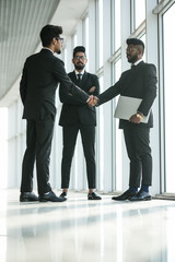 great job. two cheerful business men shaking hands while their colleagues smiling in the office back