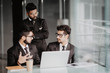 © F8  \ Suport Ukraine - Combining their expertise. Youngindian handsome man in eyeglasses gesturing and discussing something while his coworkers listening to him sitting at the office table