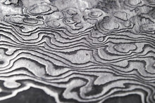 Background With Pattern Of Damask Steel. Close Up. Macro Shot Of A Damascus Knife Blade Texture. Damascus Steel Pattern. Metal And Steel Background. Damascus Steel With Original Pattern.