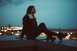 Silhouette of alone woman sitting on the roof, city on background