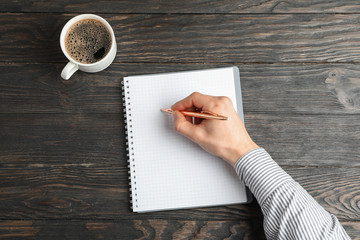 Wall Mural - Man hand with pen, copybook and cup of coffee on wooden background