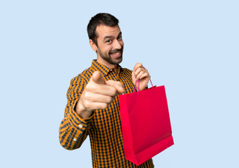 Wall Mural - Man with shopping bags points finger at you with a confident expression on isolated blue background