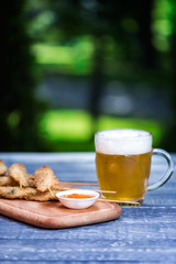 Beer snacks set. Chicken wings on sticks and mug of beer. On the cutting board and green summer background