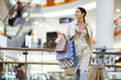 © Seventyfour - Smiling pretty young woman in coat carrying many shopping bags and going around shops and boutiques in mall