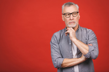 Wall Mural - Portrait of a mature serious businessman wearing glasses isolated against red background. Happy senior man looking at camera with copy space. 