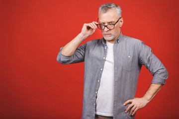 Wall Mural - Portrait of a mature serious businessman with crossed hands wearing glasses isolated against red background. Senior man looking at camera with copy space. 