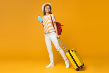 Wall Mural - Young female tourist standing with suitcase and backpack, isolated on yellow background. Travel concept