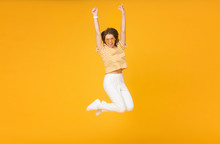 Cheerful Positive Girl Jumping In The Air With Raised Fists If She Is Winner, Isolated On Yellow Background