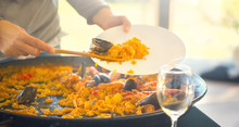 Paella. Traditional Spanish Food. Person Putts Seafood Paella From The Fry Pan To Plate. Paella With With Mussels, King Prawns, Langoustine And Squids