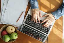 High-angle View Shows A Woman's Hands Are Typing On Laptop . .which Has Papers And Fruits Put On The Table At The The Sun Shines Light.