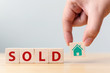 © Monster Ztudio - Hand holding wood cube block with icon house and word SOLD. Property investment and house mortgage financial concept