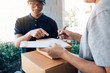 © wutzkoh - Delivery young man standing at the door of home and carrying parcels for young male to signing.