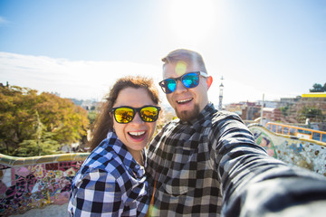 Wall Mural - Funny young couple looking at camera taking photo with smart phone smiling in Park Guell, Barcelona, Spain.