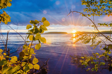 Wall Mural - sunset, sunrise over the river through the foliage with rays and highlights against the cloudy sky.
