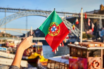 Portuguese flag as a symbol of Portugal on the background of the bridge Ponte de Dom Luis I on embankment near the river Doure in Porto