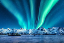Aurora Borealis Above The Snow Covered Mountains In Lofoten Islands, Norway. Northern Lights In Winter. Night Landscape With Polar Lights, Snowy Rocks, Reflection In The Sea. Starry Sky With Aurora