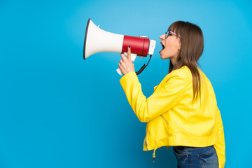 Young woman with yellow jacket on blue background shouting through a megaphone