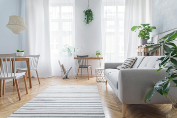 modern scandinavian living room with design furniture, grey sofa, plants, bamboo bookstand and woode