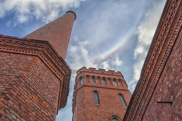 Vintage pipe and red brick buildings. Rainbow in the clouds.