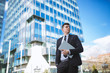 © Novak - Businessman standing with laptop against building