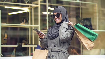 Attractive smiling female in hijab shopping and chatting on phone with friend