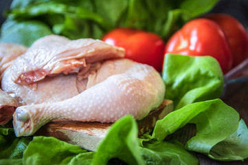 Wall Mural - Raw chicken legs on cutting board and tomato and lettuce on wooden table