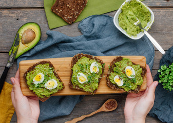 Wall Mural - Female hands holding homemade sandwiches with avokado, quail eggs and radish sprouts